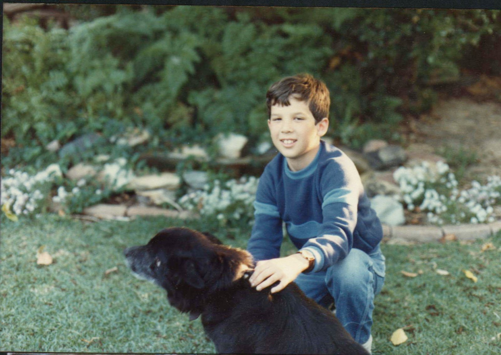Mike as a boy, kneeling on the grass with Ranger, a black dog