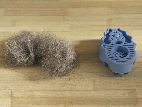 Blue KONG ZoomGroom rubber grooming brush beside a pile of brushed-out fur
